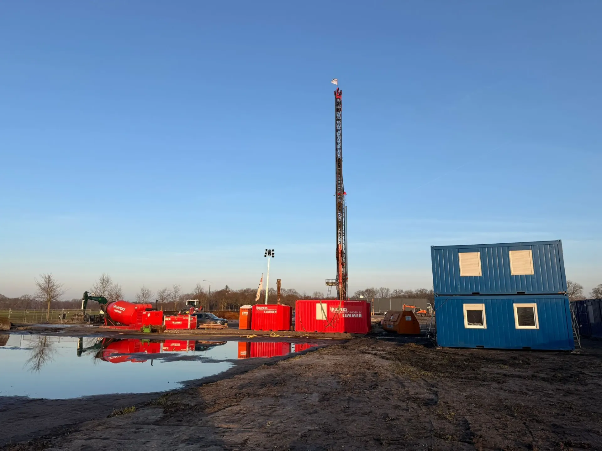 Bouwplaats met blauwe containers en rode machines bij zonsopgang.