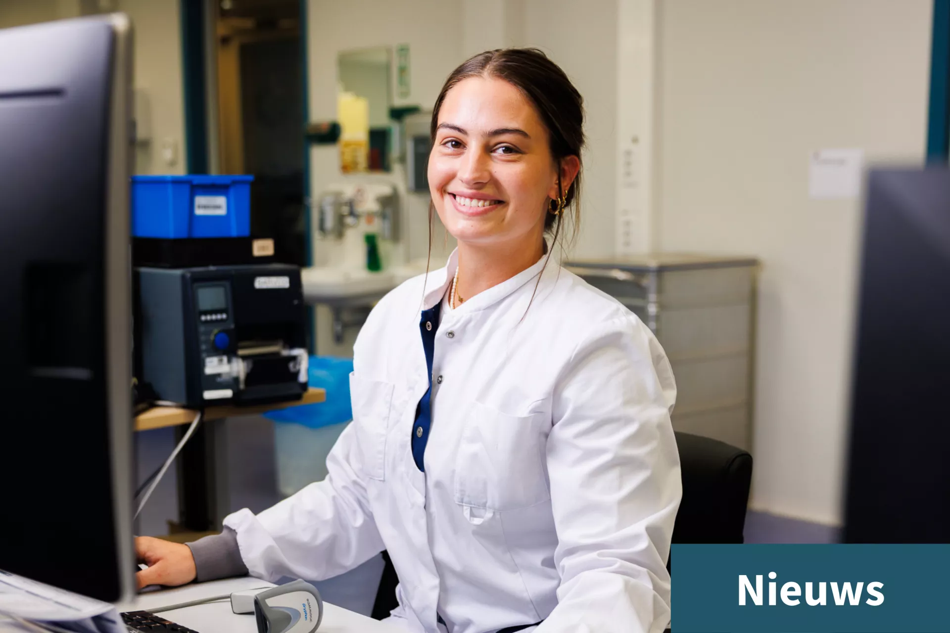 Vrouw in een laboratoriumjas achter een computer, lachend.